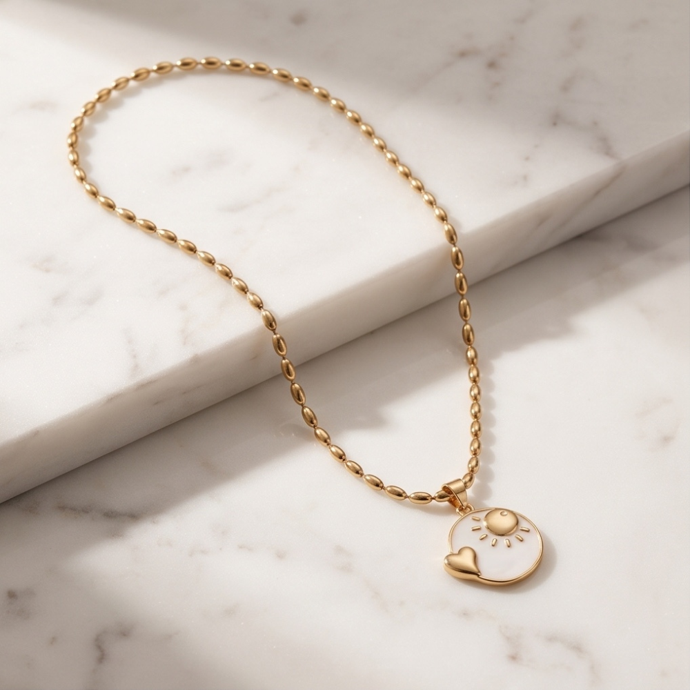Gold sun and heart pendant necklace displayed on white marble background